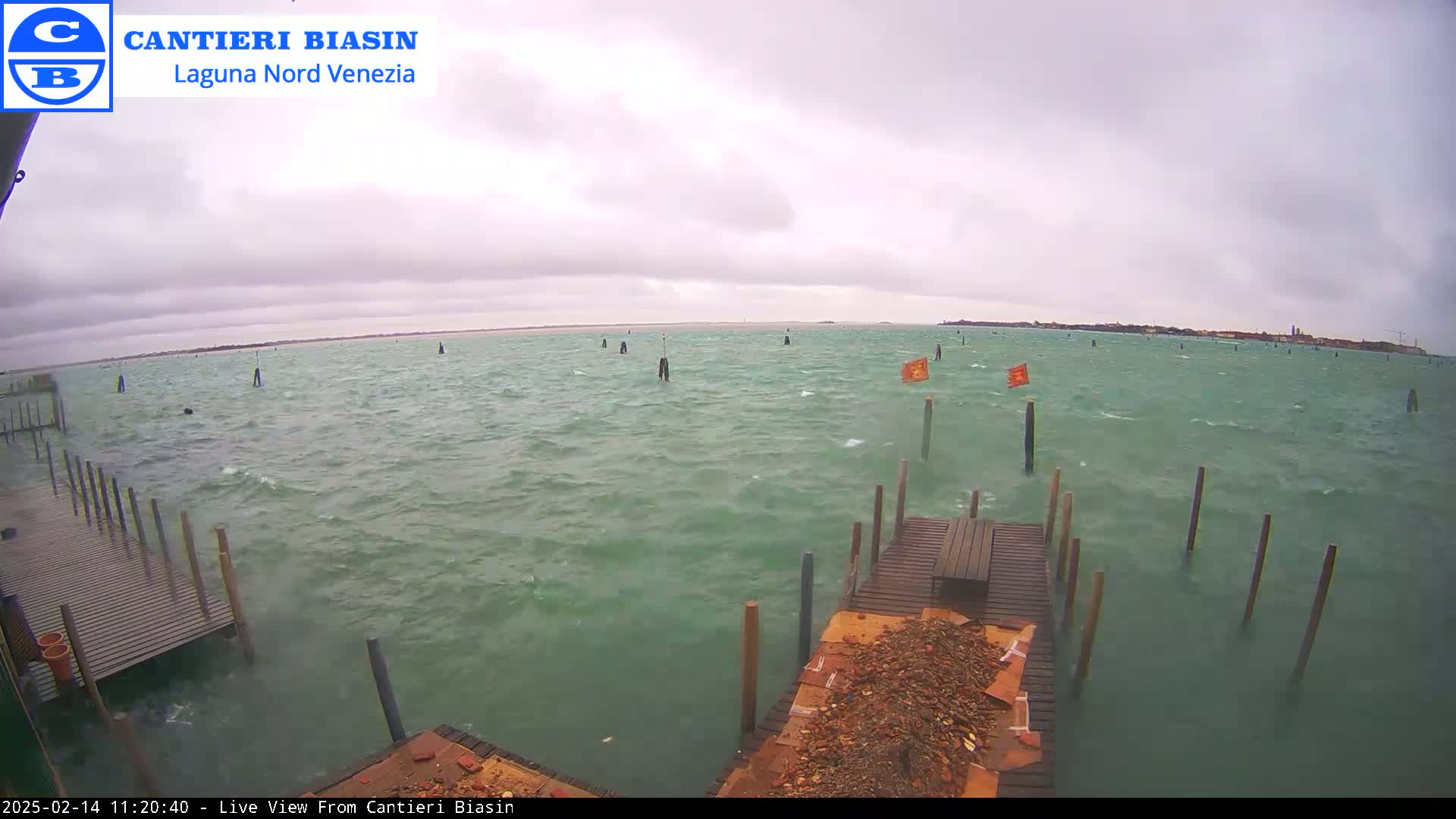 A choppy body of water with several wooden posts and a dock in the foreground under an overcast sky.