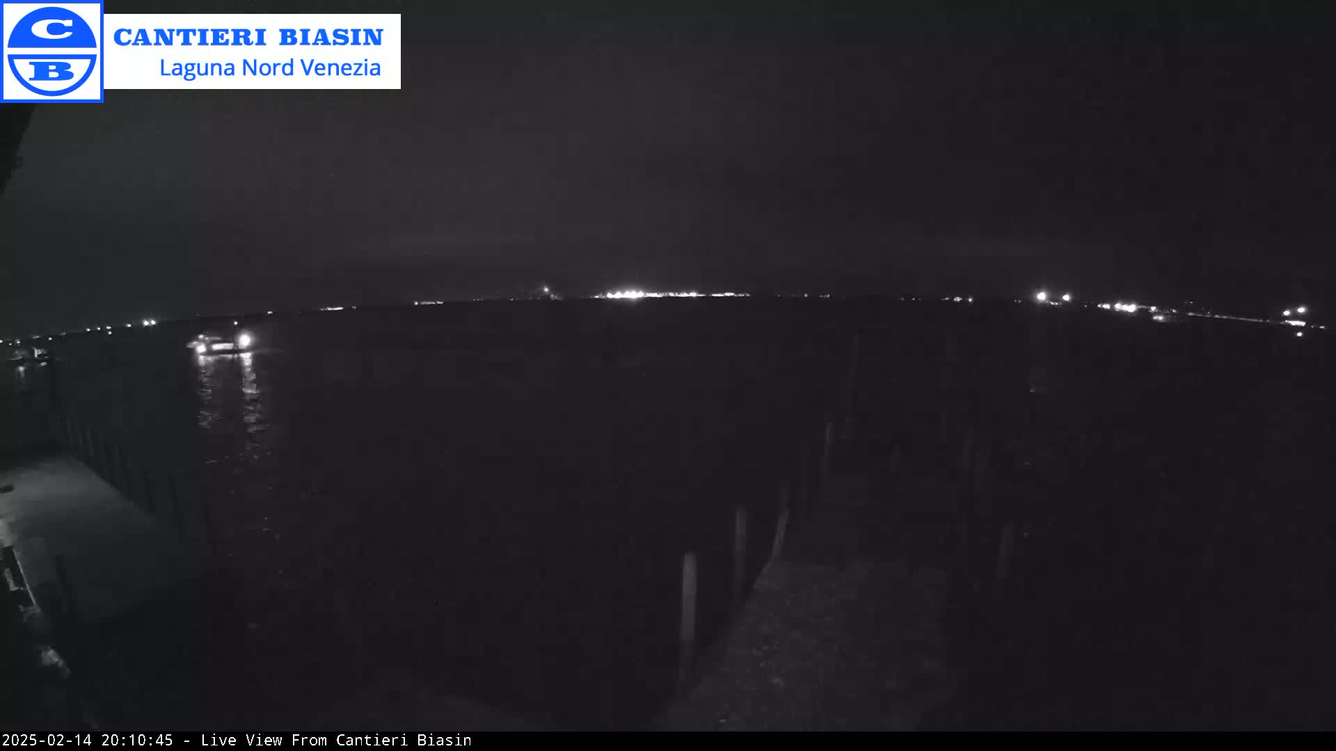 A nighttime view of dark water with distant lights on the horizon, and a dark structure visible in the foreground.