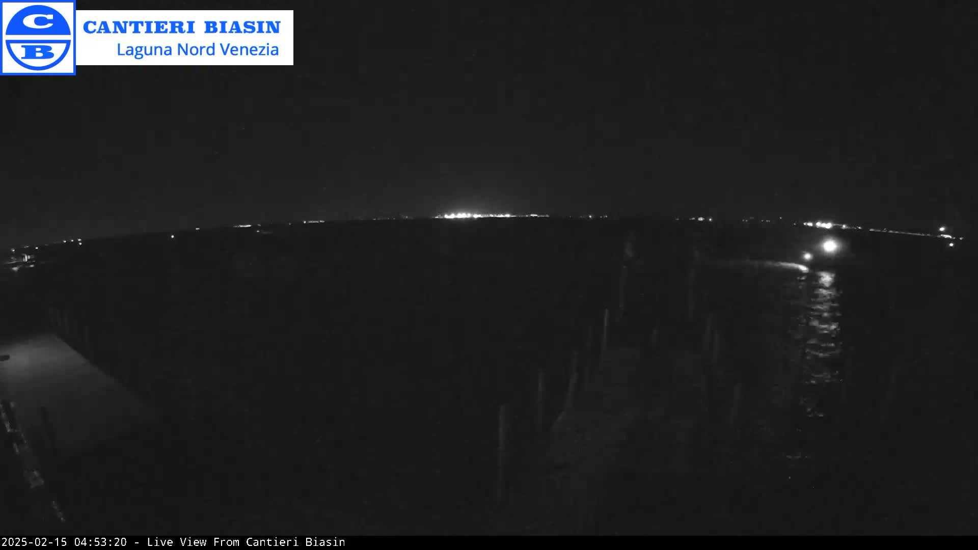 A nighttime view of a dark body of water with a distant, faintly lit shoreline.