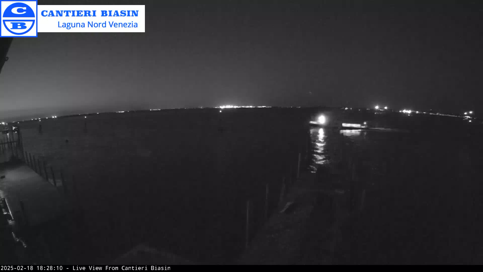 A nighttime view of a dark body of water with a distant shoreline faintly illuminated by lights.