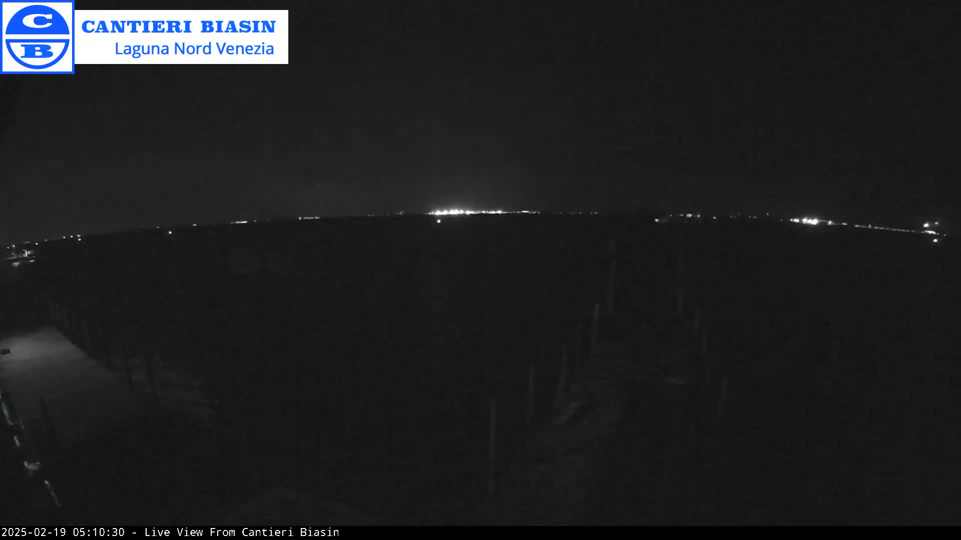 A nighttime, dark view of a flat landscape with a distant line of lights on the horizon.