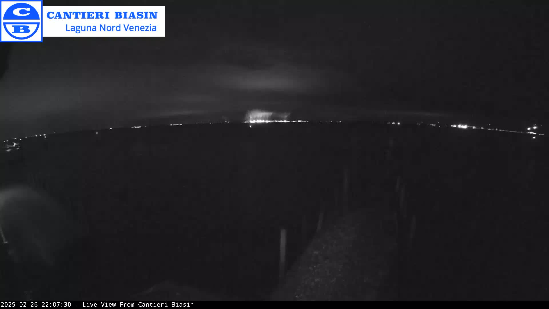 A nighttime, dark view of a distant line of lights on the horizon under a cloudy sky.