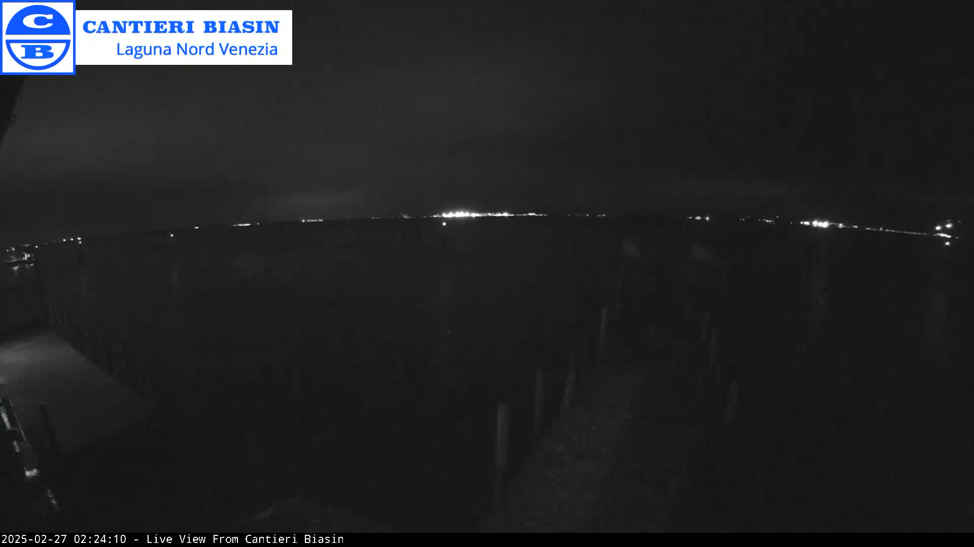 A nighttime view of a dark, flat landscape with a distant line of lights under a mostly clear sky.