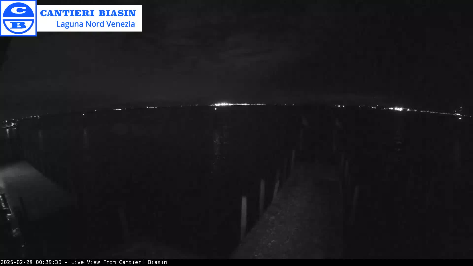 A nighttime view shows a dark landscape with a distant line of lights on the horizon under a dark sky.