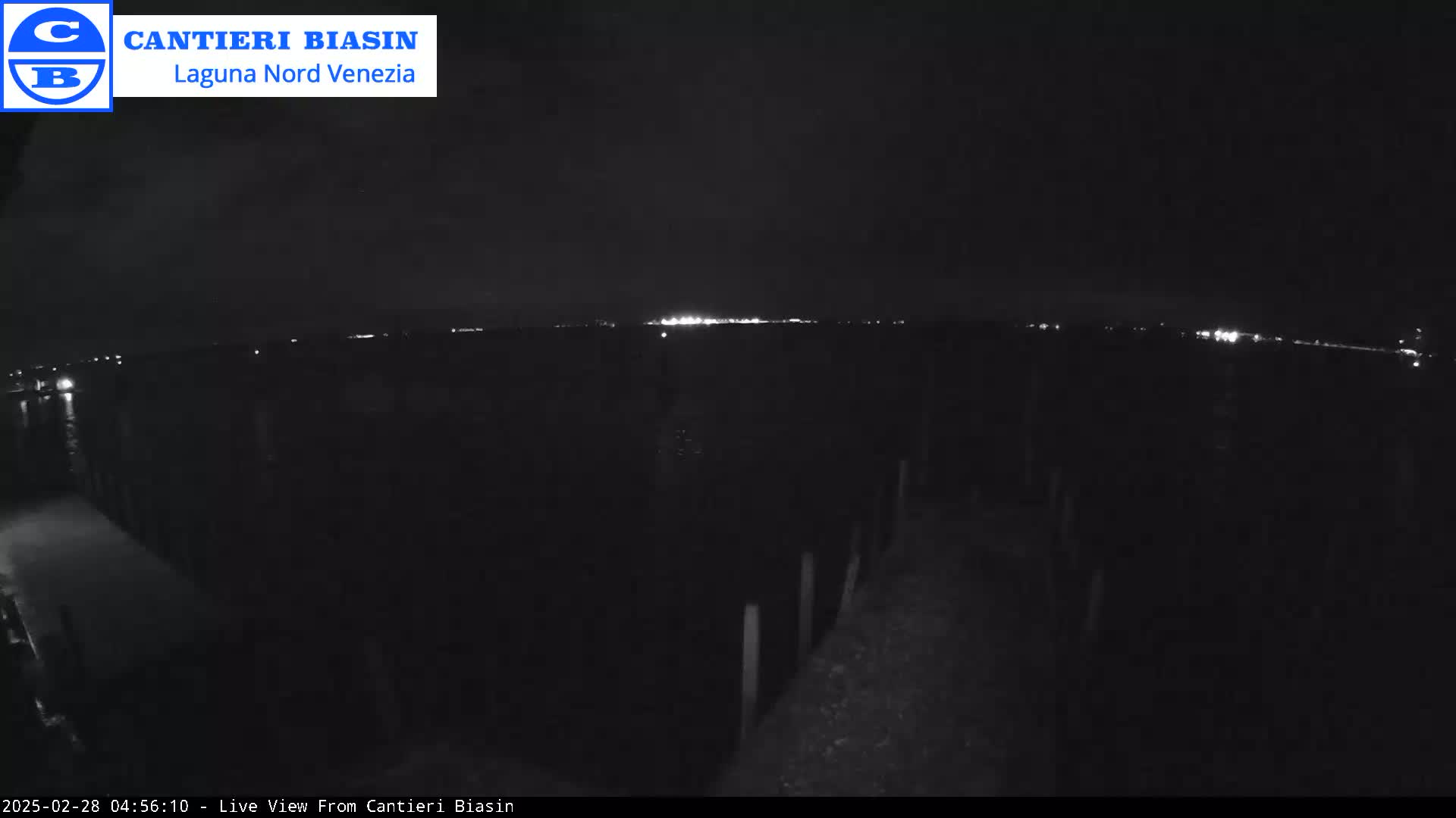 A nighttime, low-light view shows a dark body of water with a distant line of lights on the horizon.