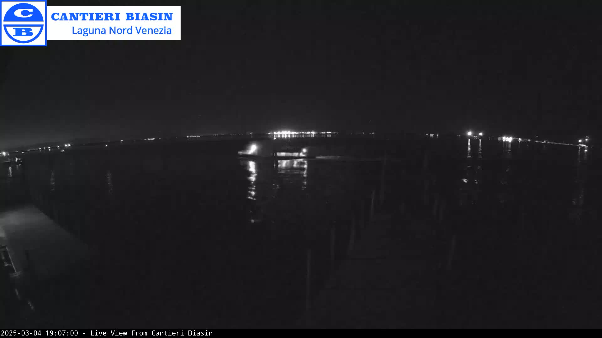 A nighttime view of a dark body of water reflecting distant lights under a clear sky.
