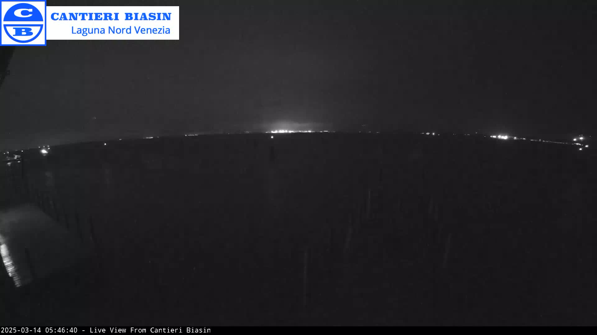 A nighttime long shot shows a dark landscape with a distant line of lights under a dark sky.