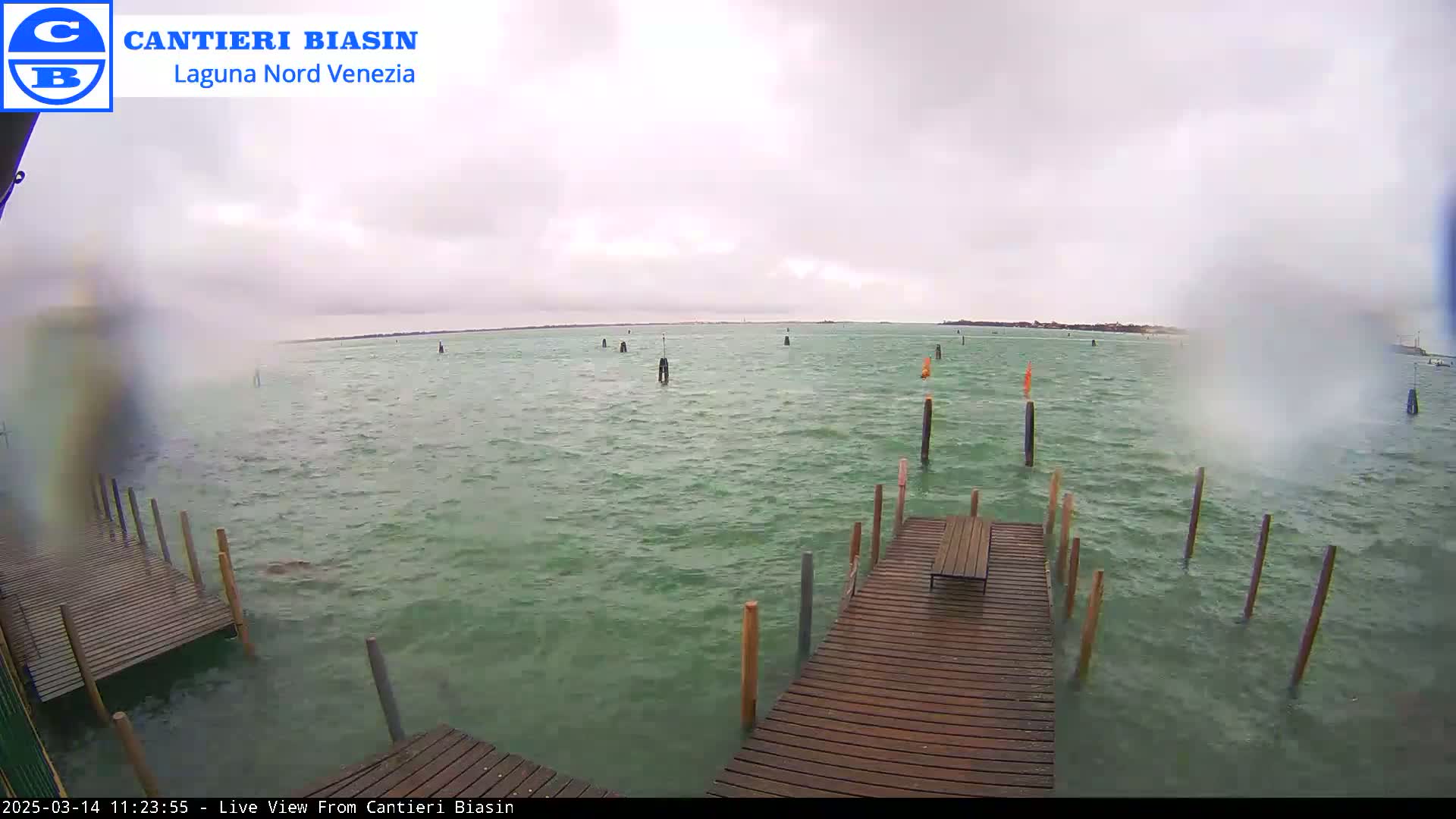 A wooden dock extends over greenish-grey water under an overcast sky with choppy waves.