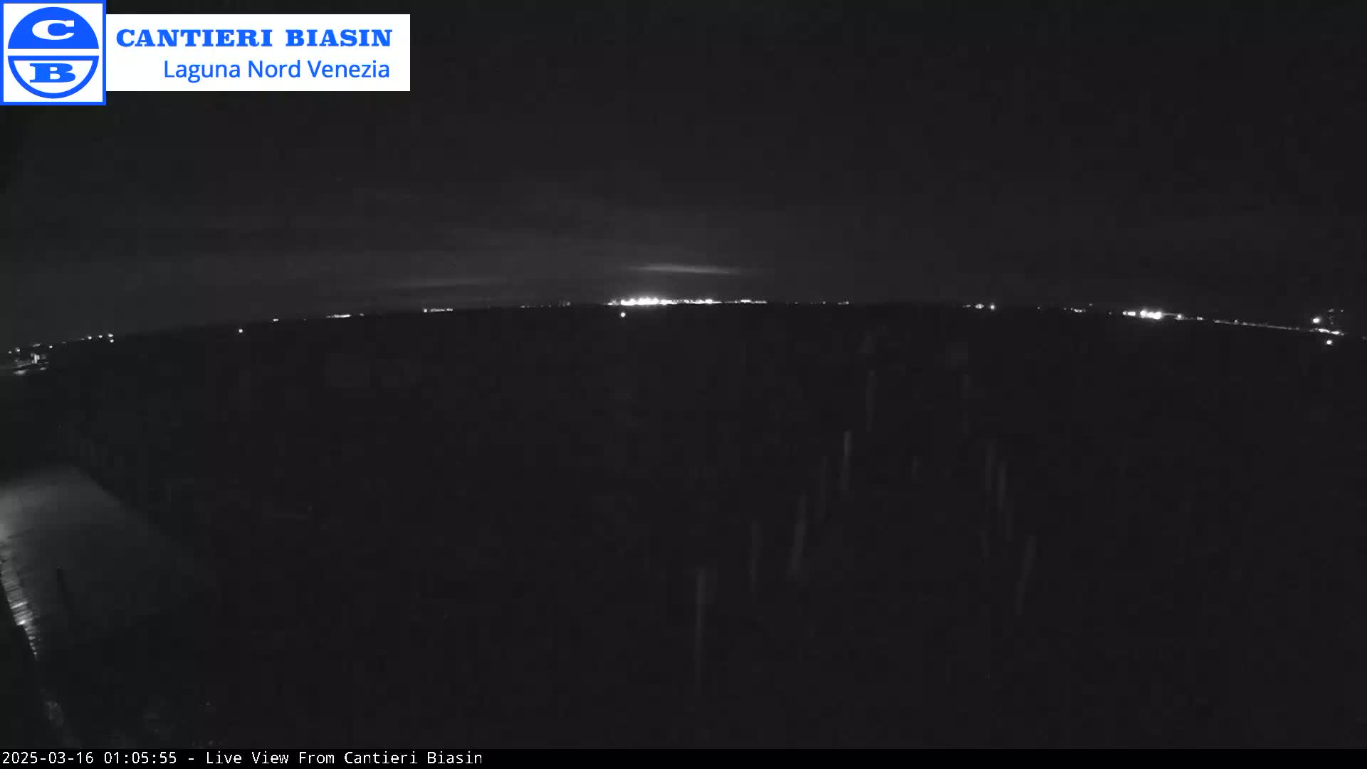 A nighttime, low-light view shows a dark landscape with a distant line of lights on the horizon.