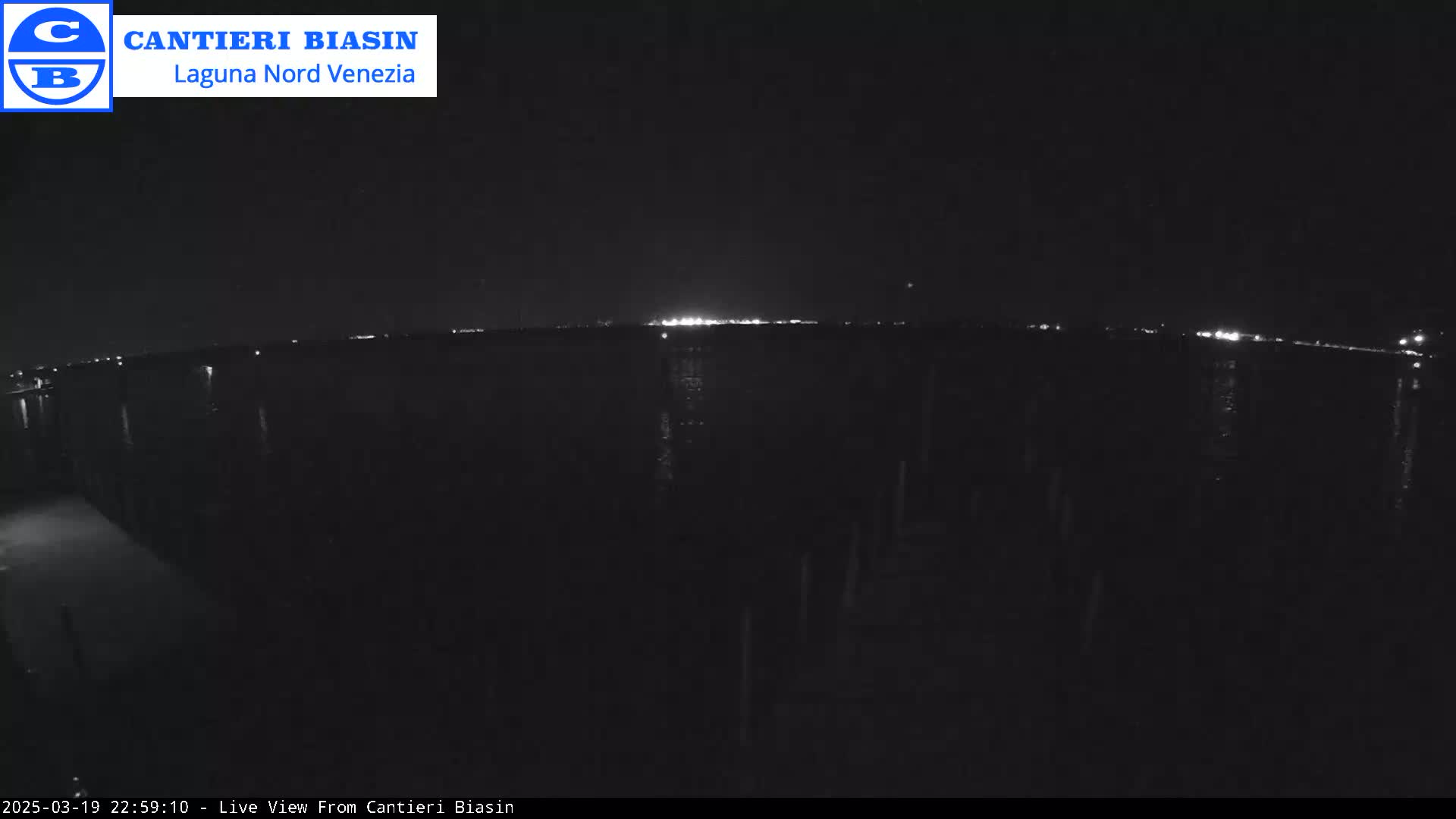 A nighttime view of a dark body of water reflecting distant lights under a clear sky.