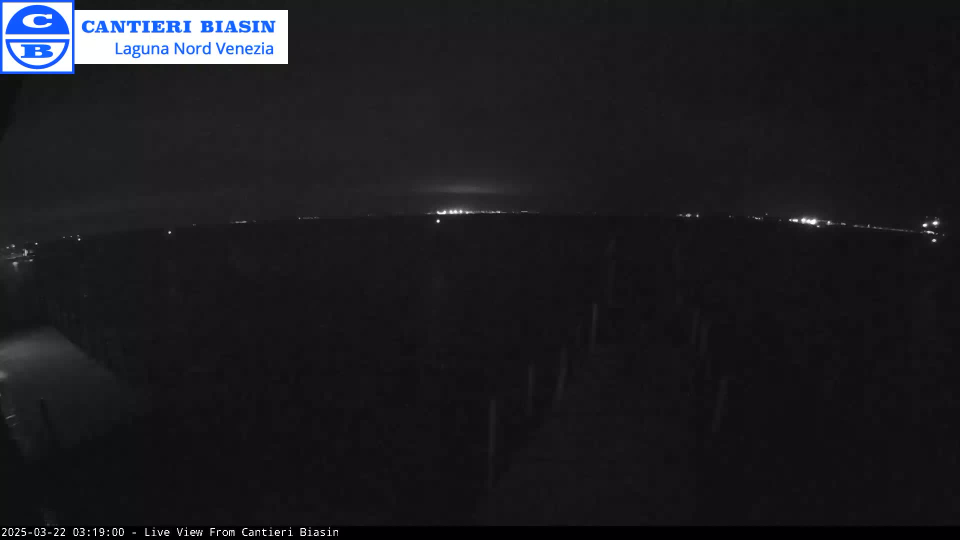 A nighttime, low-light view shows a dark landscape with a distant line of faint lights on the horizon.