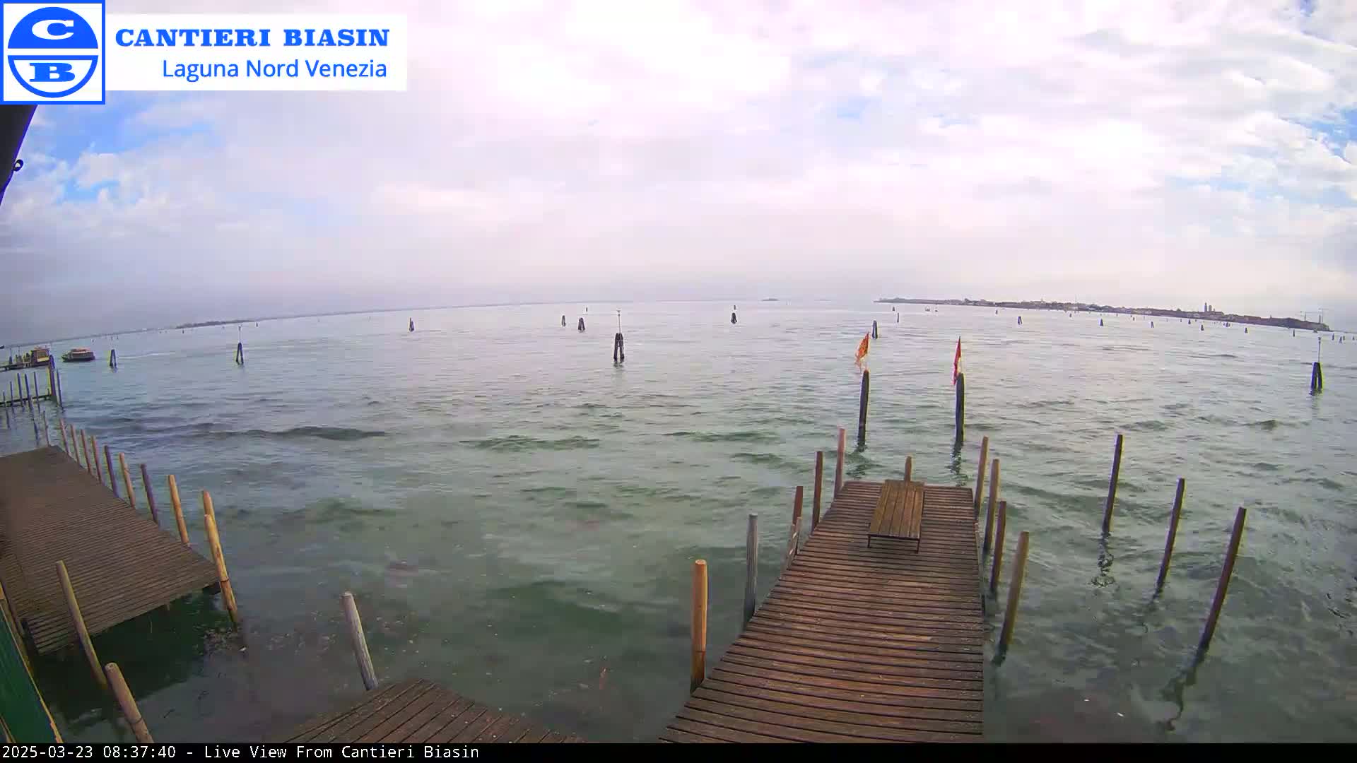 A wooden dock extends over somewhat choppy water under a partly cloudy sky, with numerous posts and markers visible in the distance.