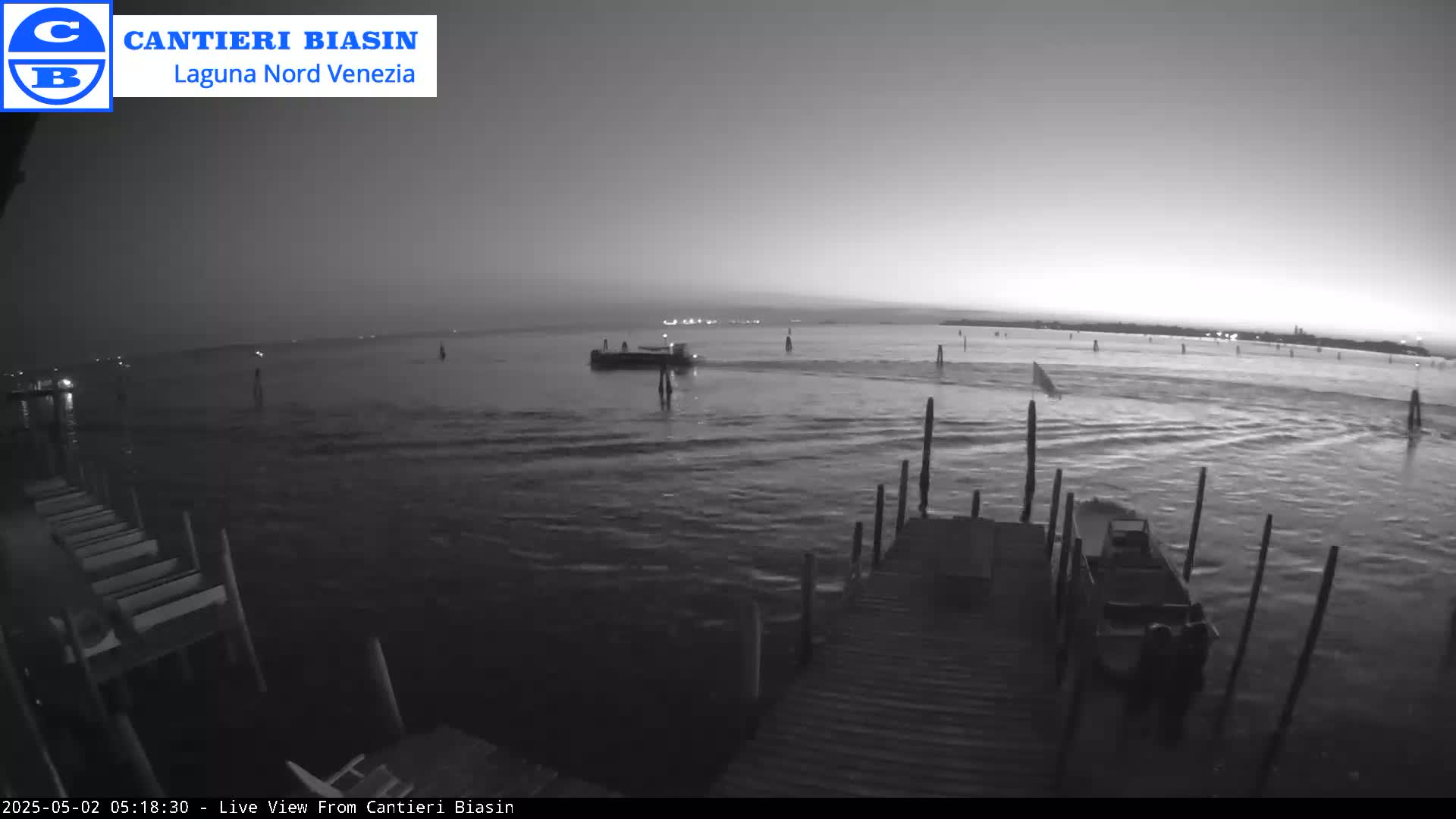 A nighttime, low-light view shows a calm body of water with several boats and a dock; one boat is close to the dock.