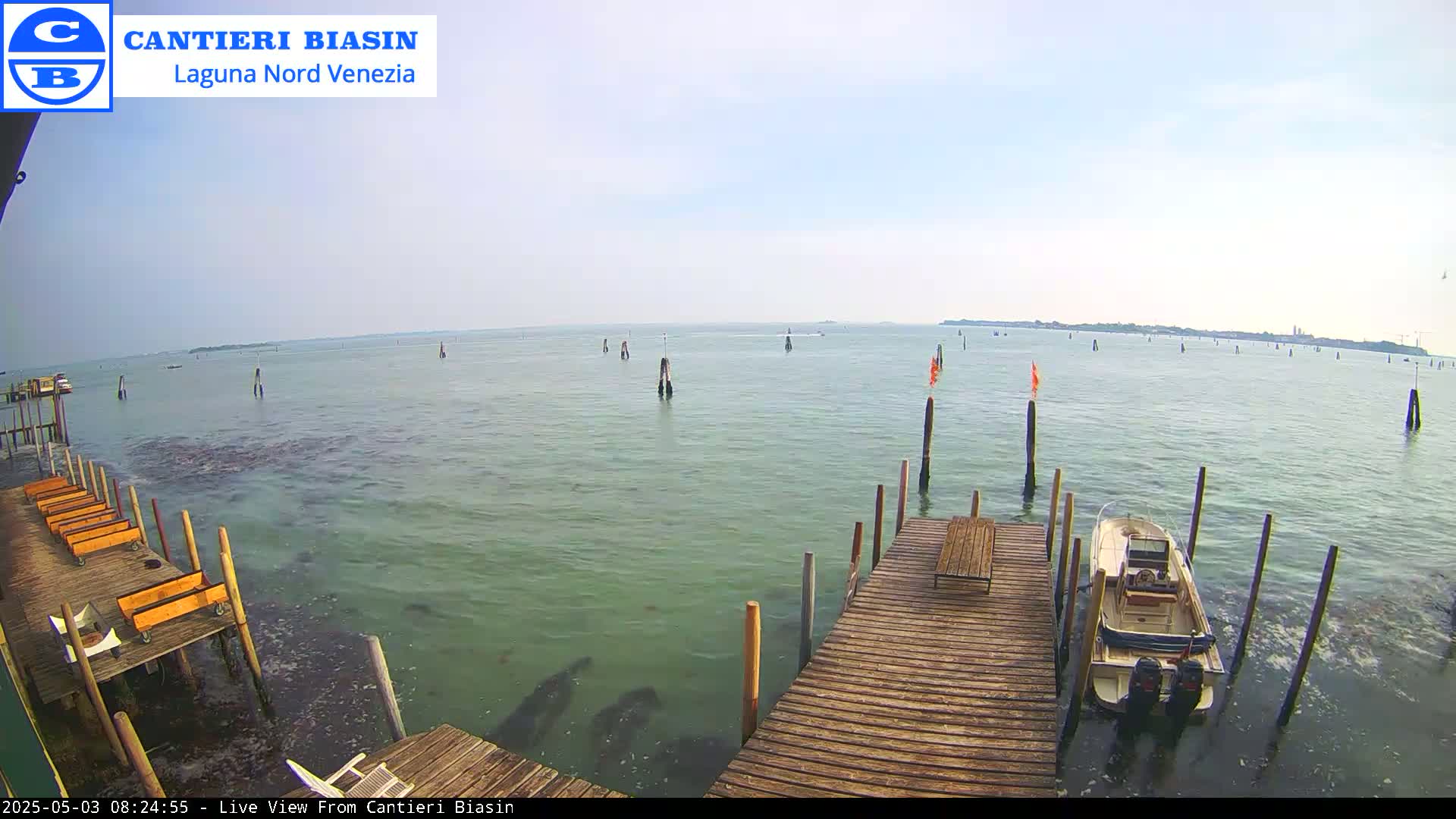 A mostly sunny day shows a calm body of water with several wooden pilings and a small boat docked at a wooden pier.