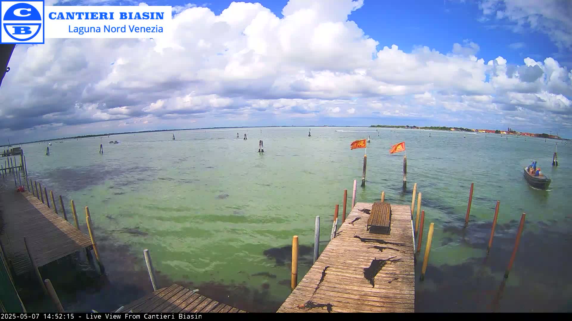 A partly cloudy day with a view of a calm body of water, wooden docks, and a small boat, seen from a wooden pier.