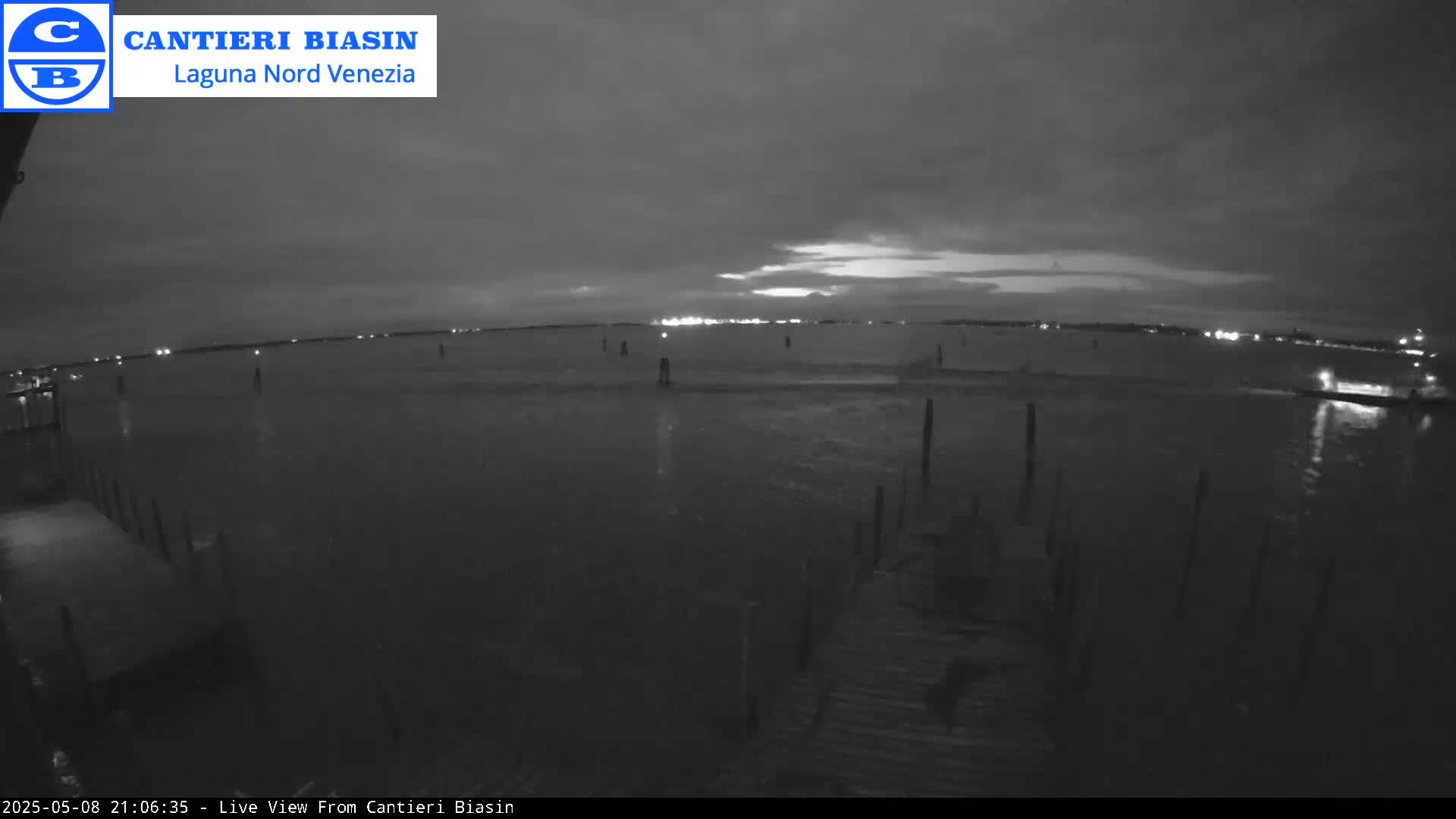 A nighttime view of a calm body of water with distant lights on the horizon under a cloudy sky.