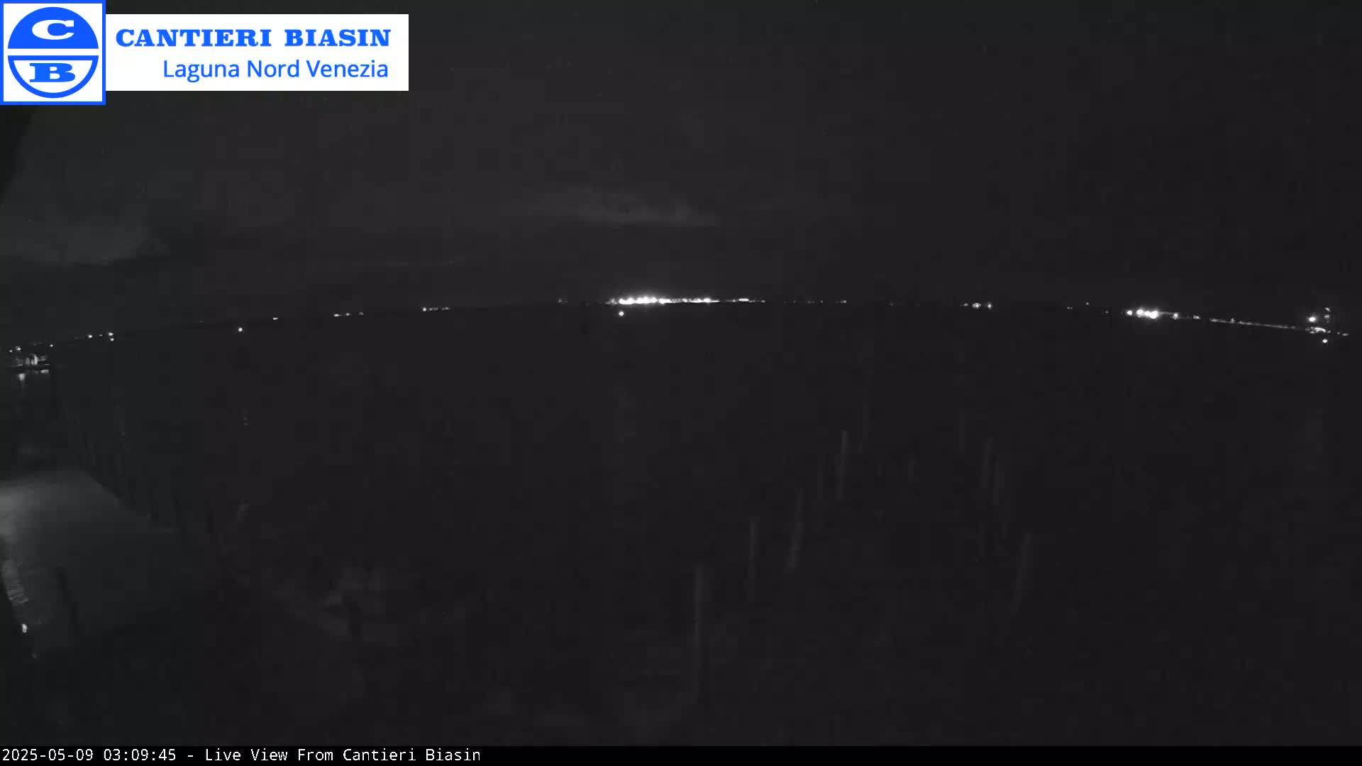 A nighttime, dark view shows a distant line of lights in the distance under a mostly clear, dark sky with a few faint clouds.