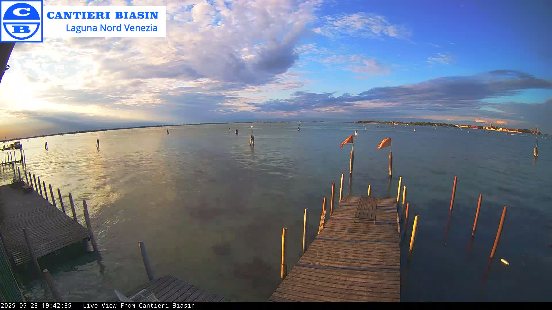 A wooden dock extends over calm water under a partly cloudy sky at sunset, with a distant shoreline visible.