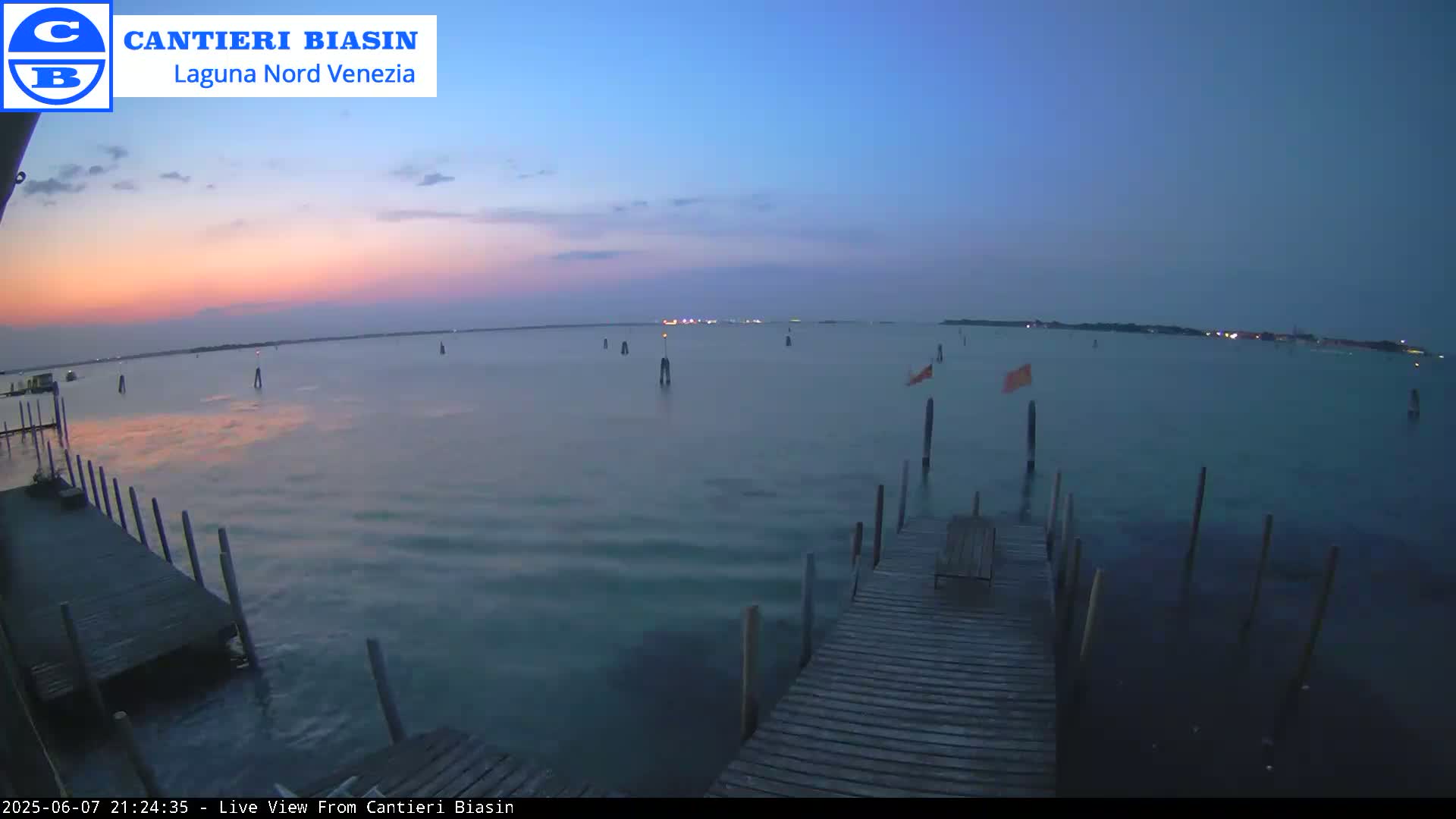 A calm body of water at dusk, showing a wooden dock extending into the water with several posts and markers visible in the distance.