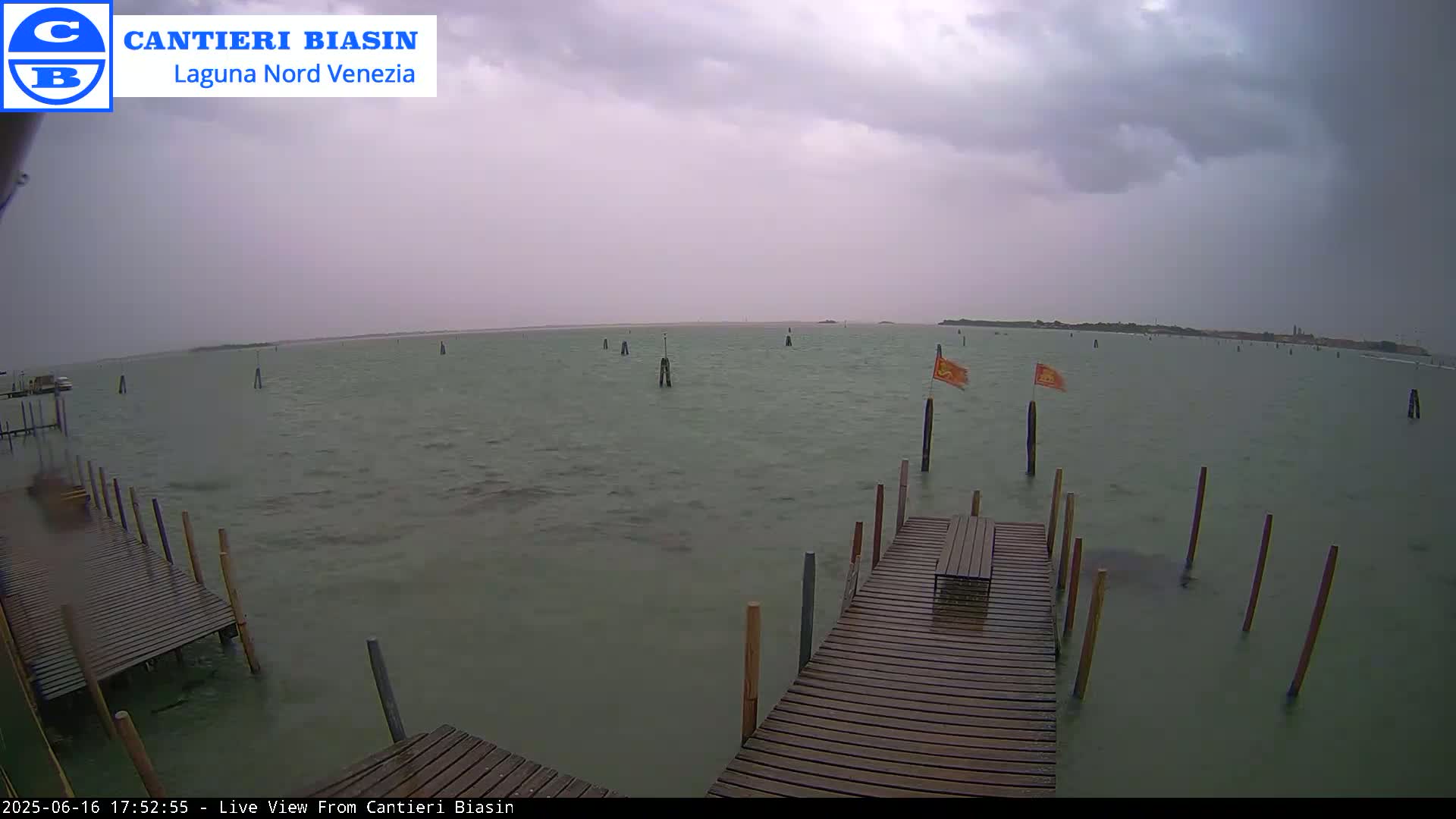 A wooden dock extends over murky water under a cloudy, possibly rainy sky, with several posts and orange flags visible in the distance.