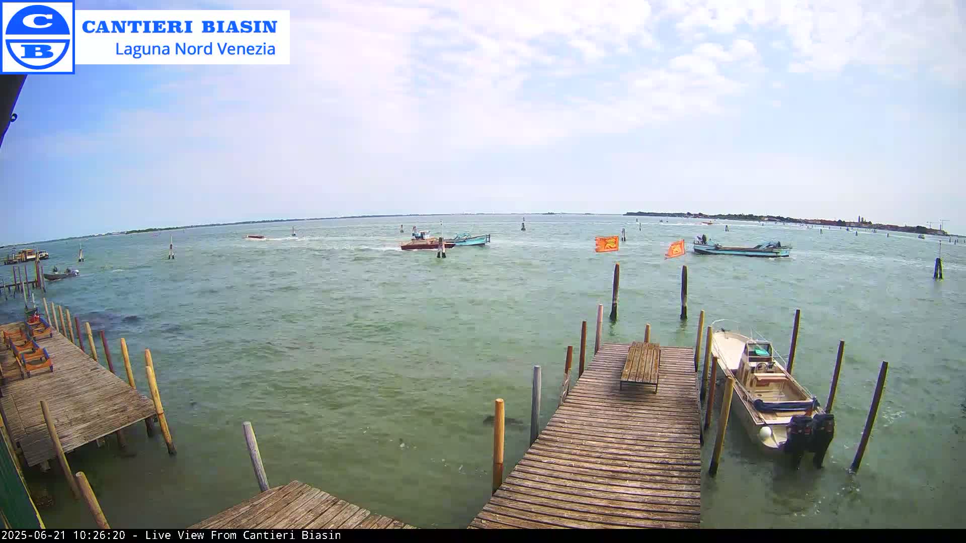 Several boats are on a body of water under a partly cloudy sky, with a wooden dock extending into the water in the foreground.