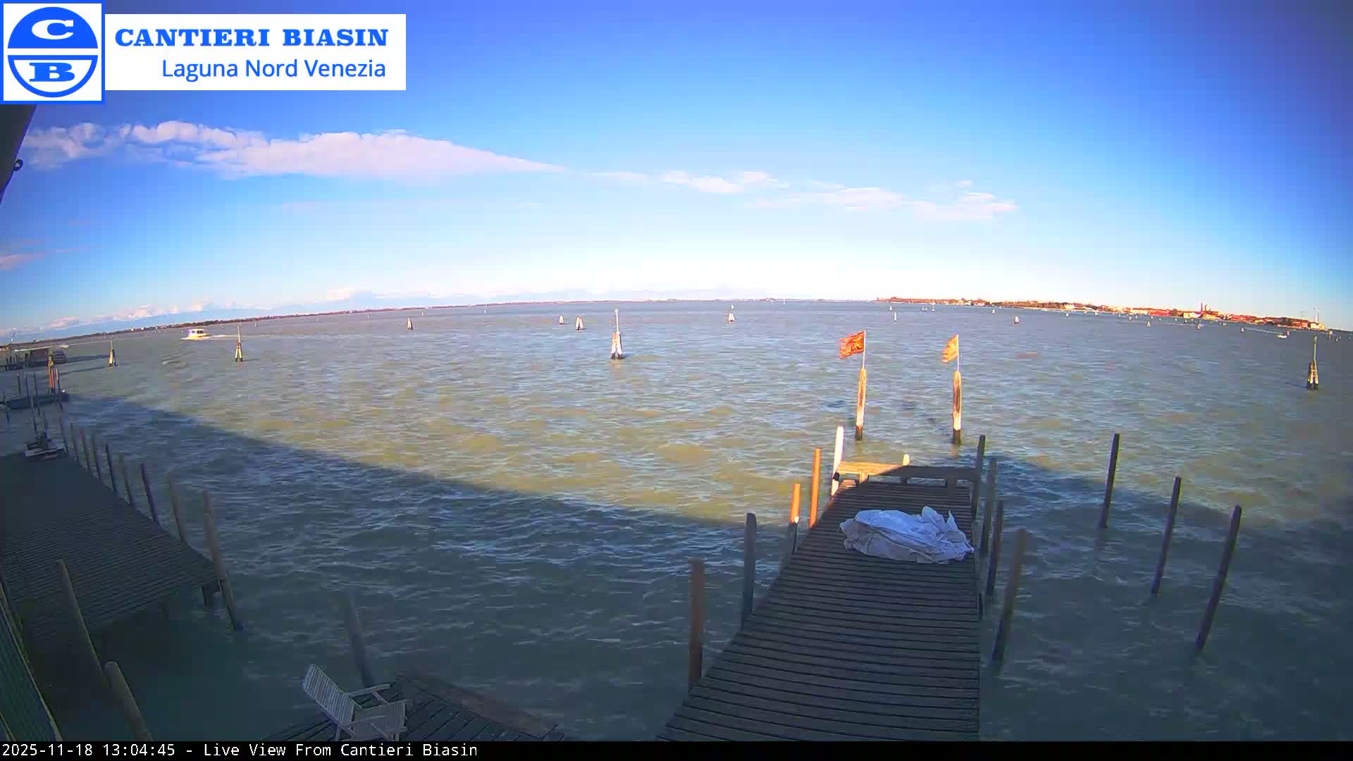 A dark, clear night scene shows a wooden dock extending into calm water, with a white tarp or cover on the dock and distant lights twinkling across the horizon.