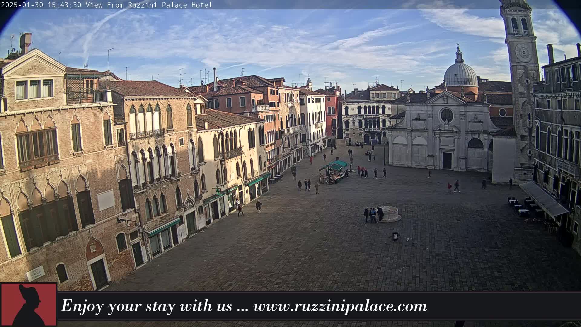 A mostly sunny day reveals a large cobblestone square in Venice, Italy, surrounded by aged buildings, a church, and a bell tower, with a few people sparsely scattered throughout.
