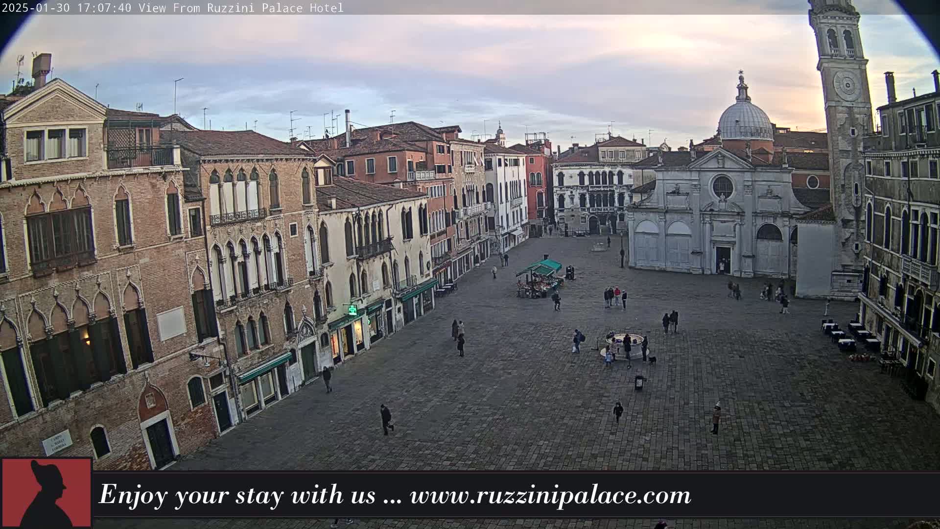 A large, mostly empty square in Venice, Italy, is surrounded by ancient brick buildings under a partly cloudy twilight sky.