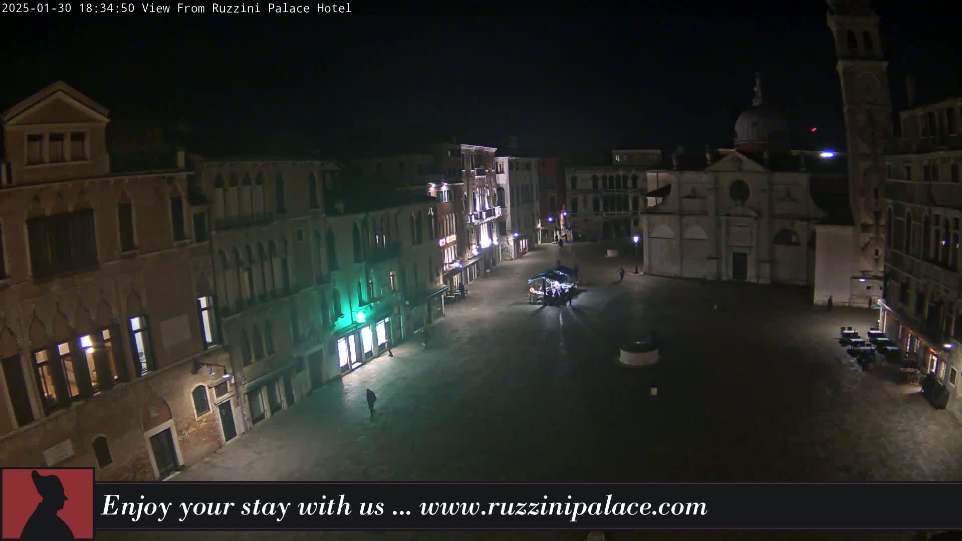 A nighttime view of a mostly empty, cobblestone plaza in Venice, surrounded by old buildings and a church, under dark skies.
