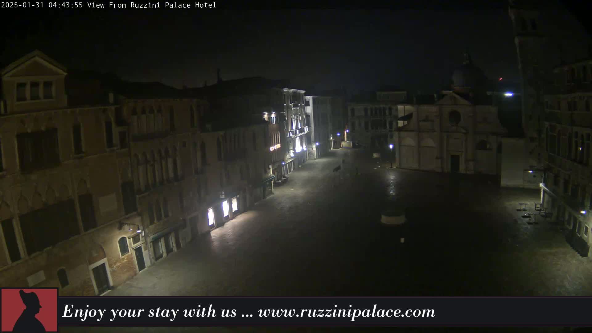 A nighttime view of a mostly empty, wet plaza in Venice, Italy, surrounded by old buildings.