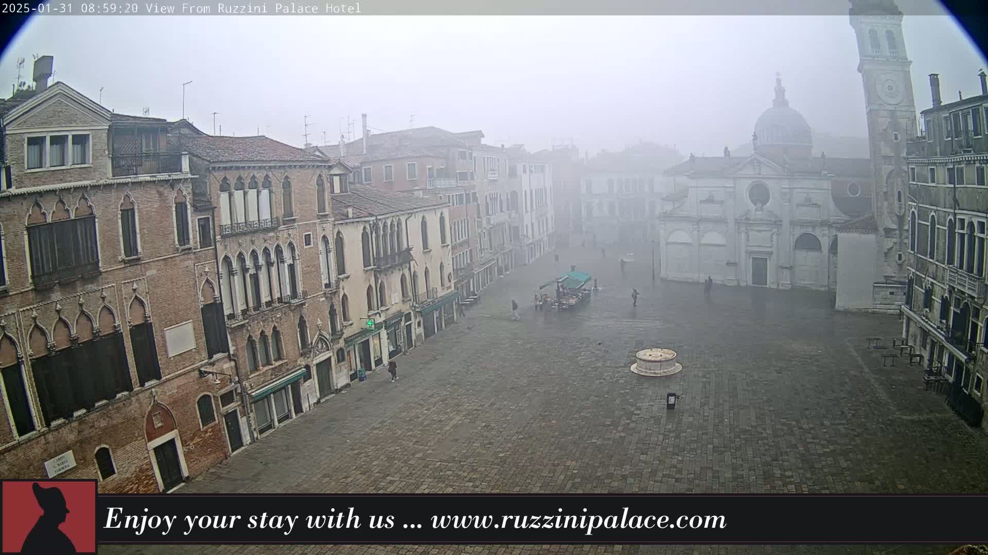 A foggy Venetian square is viewed from above, showing several historic buildings and a few sparse pedestrians.