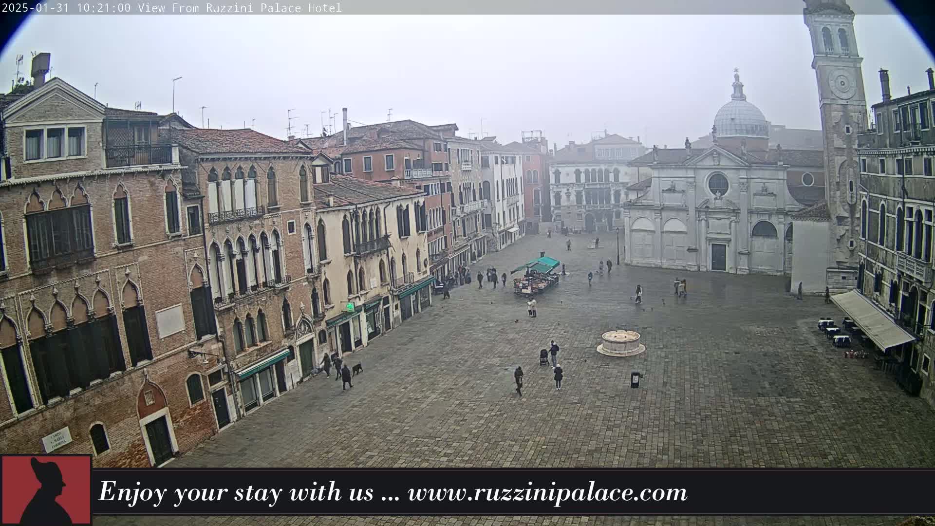 A foggy Venetian square is seen from above, showing several historic buildings and a few pedestrians.