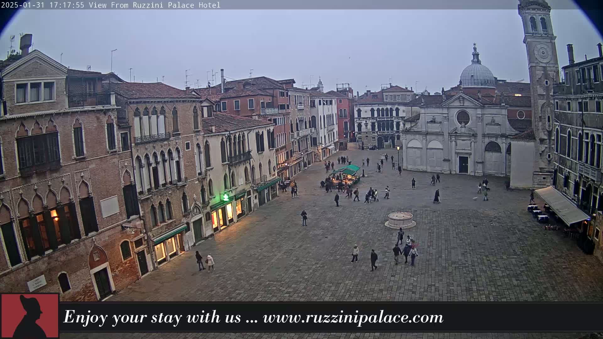 A large, mostly empty cobblestone square in Venice is surrounded by old, brick buildings under a gray, overcast sky.