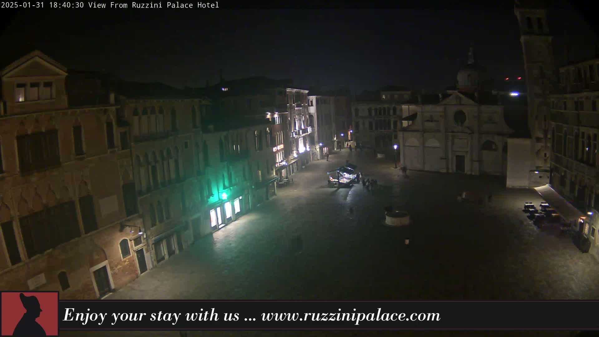 A nighttime view of a mostly empty plaza in Venice, Italy, surrounded by old buildings, with a church prominently featured.