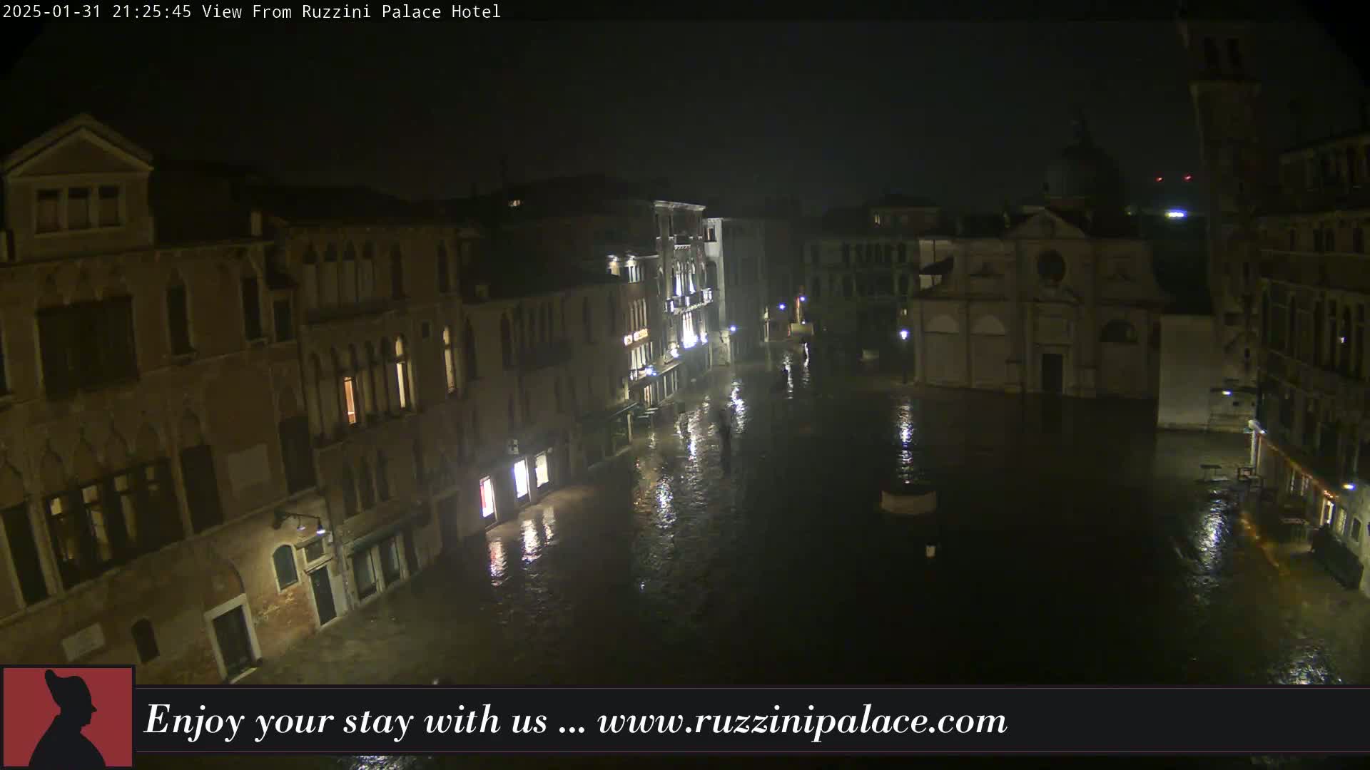 A nighttime view of a flooded Venetian square, surrounded by old buildings under a foggy sky.