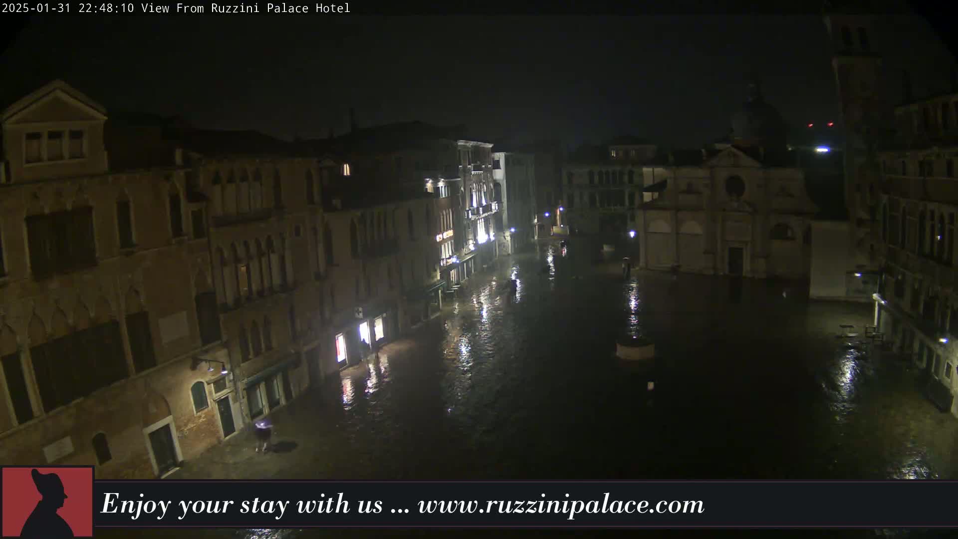 A nighttime view of a flooded Venetian square, surrounded by old buildings under a dark, possibly rainy sky.
