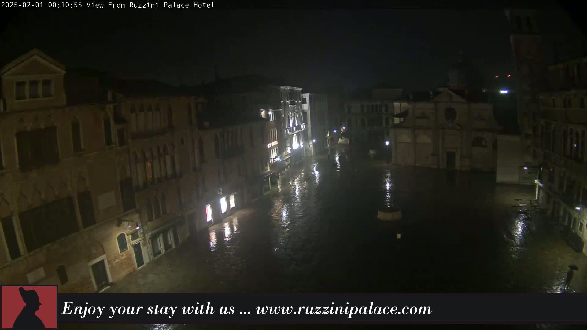 A nighttime view of a flooded plaza in Venice, Italy, surrounded by historic buildings under rainy conditions.
