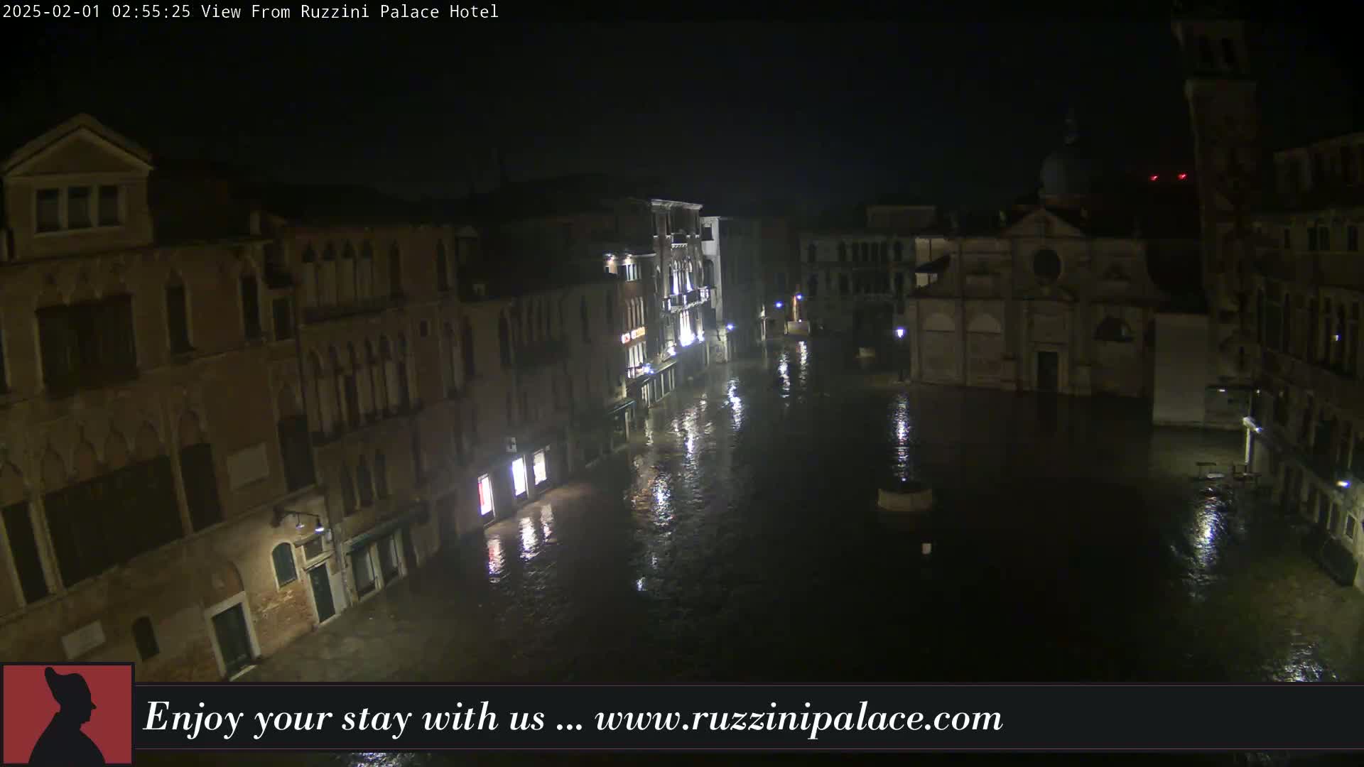 A nighttime view of a flooded Venetian square, surrounded by buildings, under a dark sky.