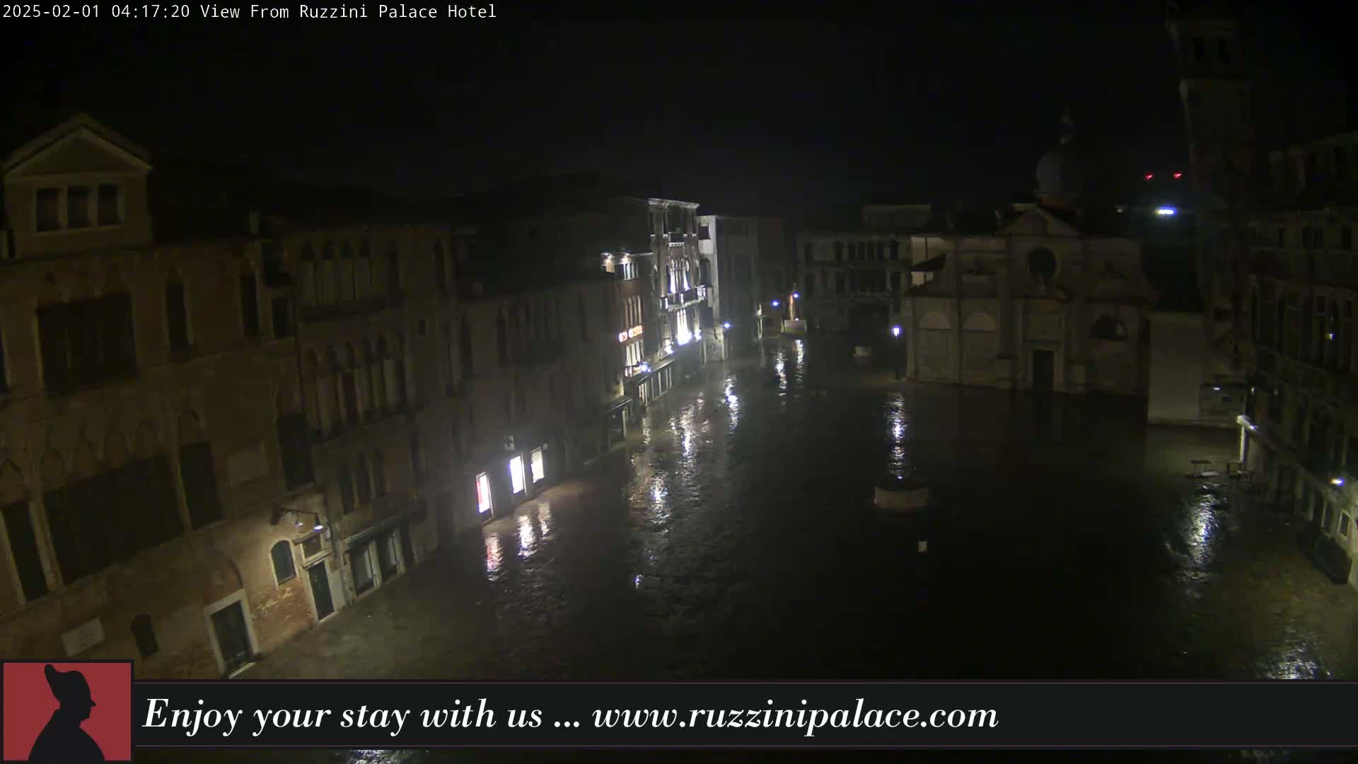 A nighttime view of a flooded Venetian piazza, with buildings lining the square and reflecting in the dark water.