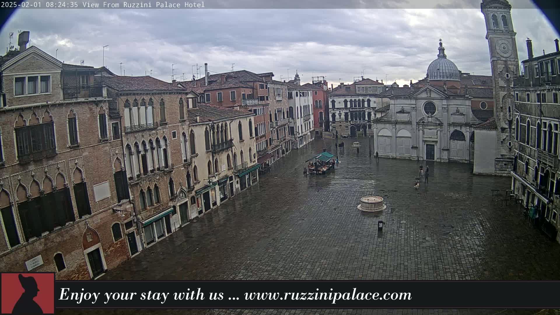 A wet, cobblestone square in Venice is surrounded by old, brick buildings under a cloudy sky.