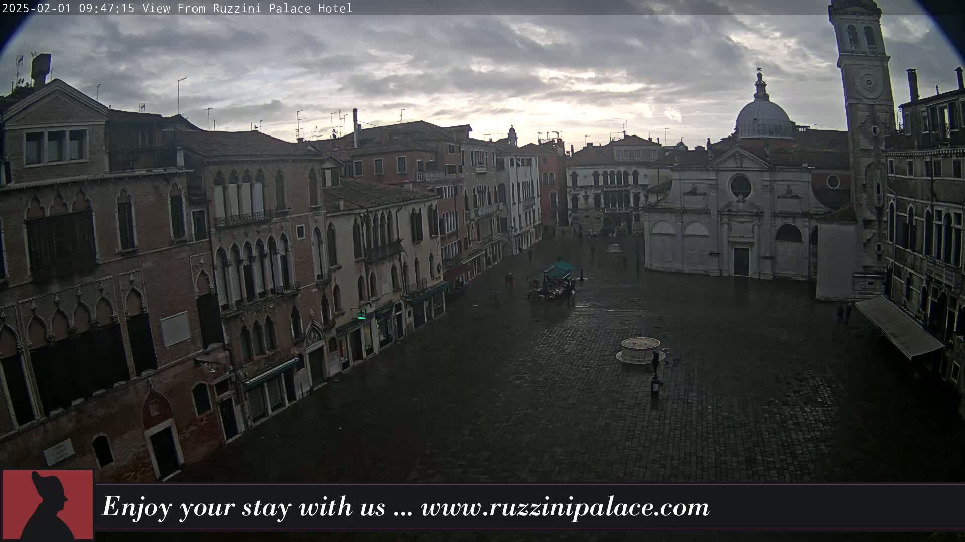 A wet, overcast Venetian square is surrounded by old, tall buildings, one of which has a dome and bell tower.