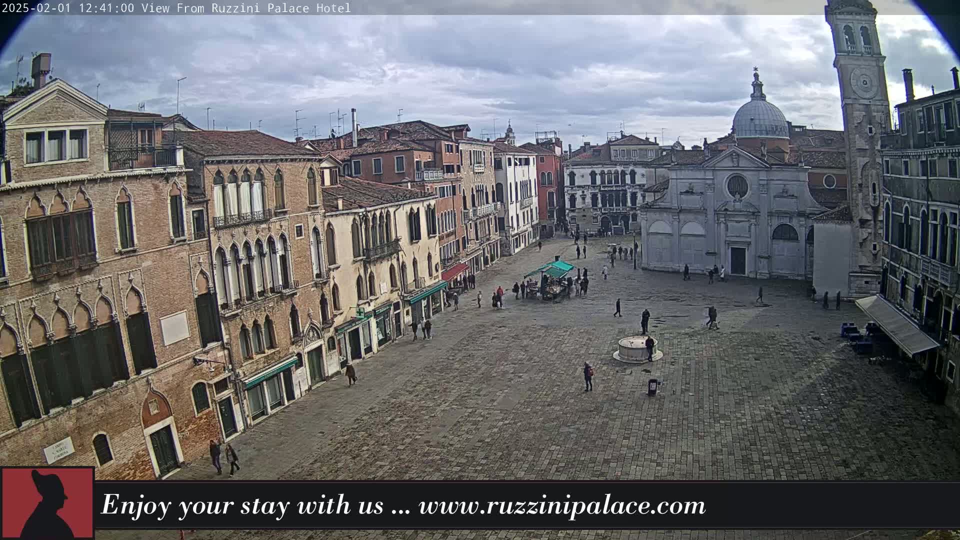 A mostly cloudy day reveals a large, paved square in Venice, surrounded by aged buildings and a few pedestrians.
