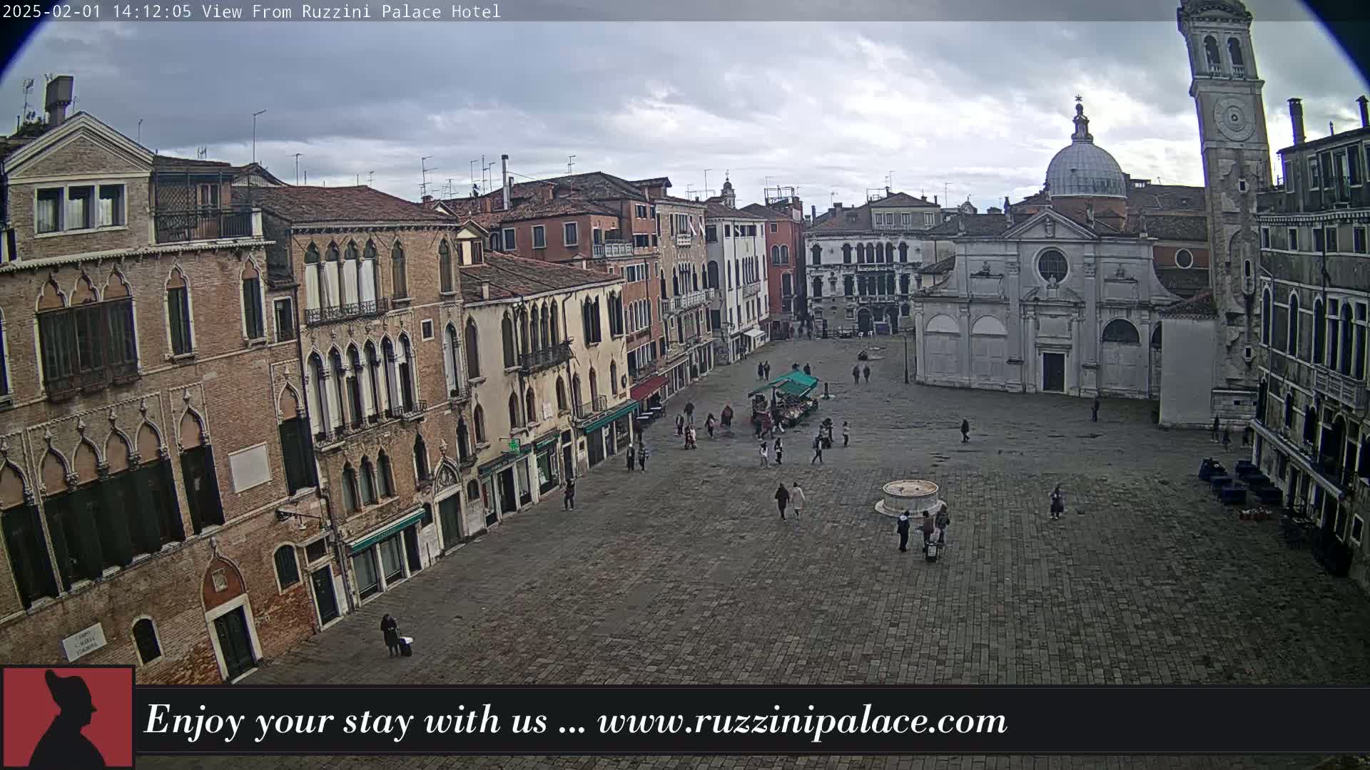 A large, sparsely populated stone plaza in Venice is viewed from above on an overcast day, surrounded by old, multi-story buildings.
