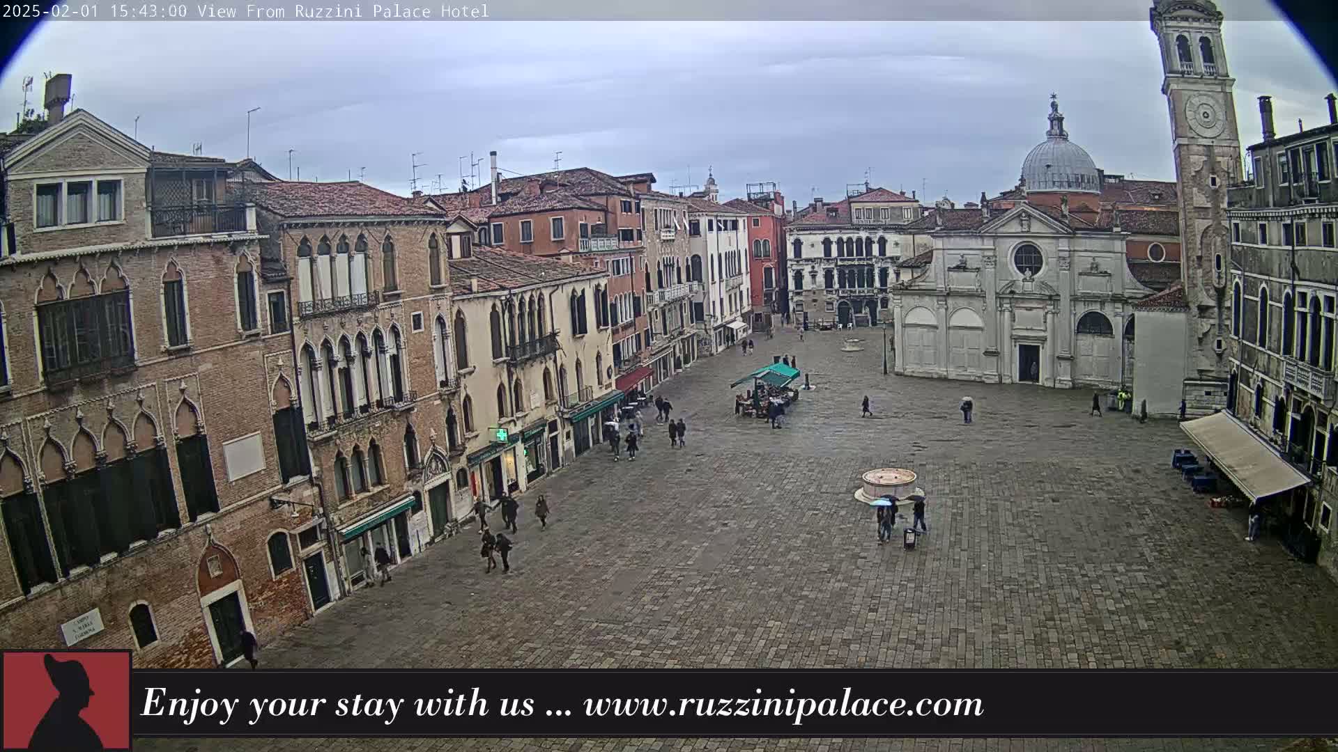 A large, cobblestone square in a city, surrounded by historic buildings under an overcast sky, with a few people walking around.