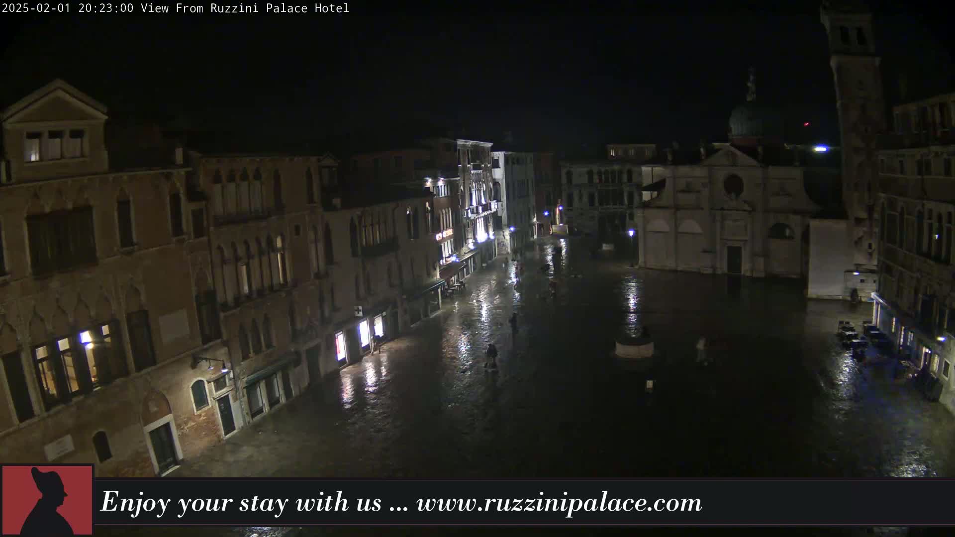 A nighttime, flooded Venetian square is surrounded by historic buildings under a dark sky.
