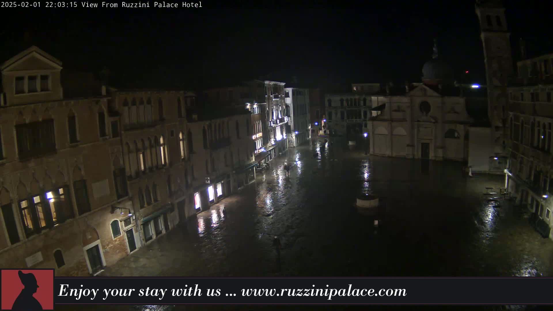 A nighttime, high-angle view of a flooded Venetian square surrounded by old buildings under dark, possibly rainy conditions.