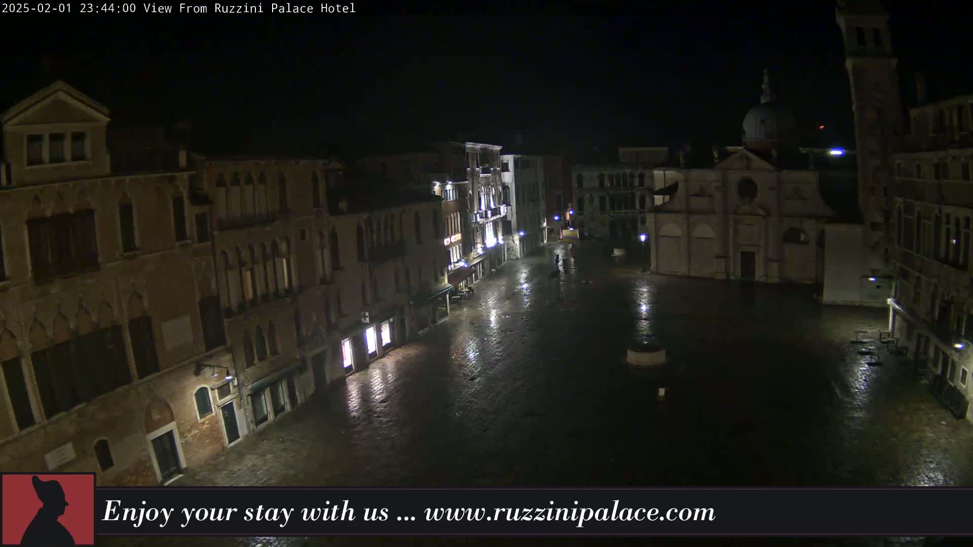A nighttime view of a wet, empty plaza surrounded by old buildings, one of which has a dome.
