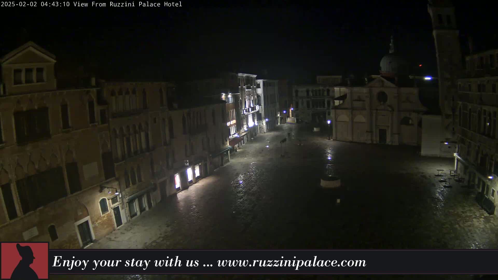 A nighttime, wet view of a cobblestone square in Venice, Italy, surrounded by old buildings, one of which is a church.