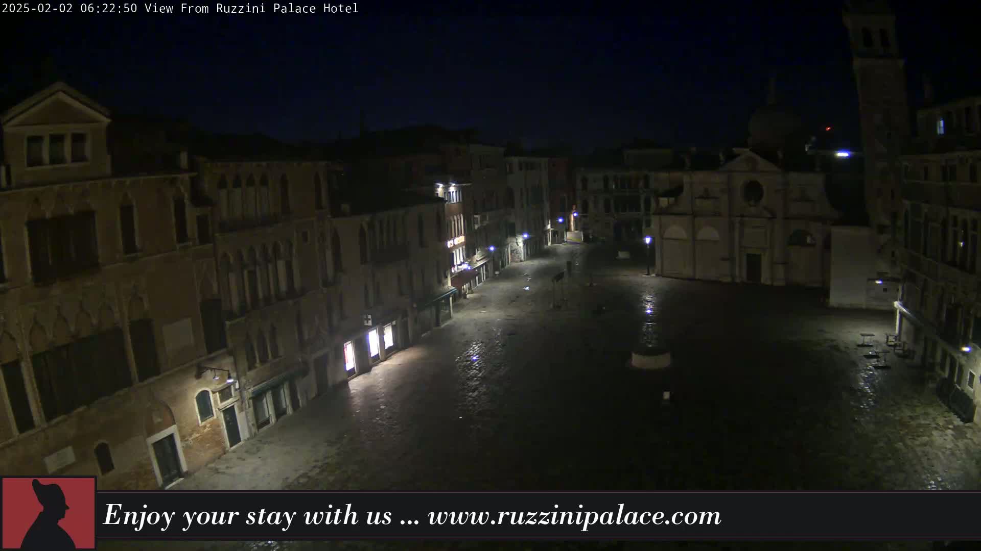 A nighttime view of a dimly lit, empty cobblestone square in Venice, surrounded by old buildings.