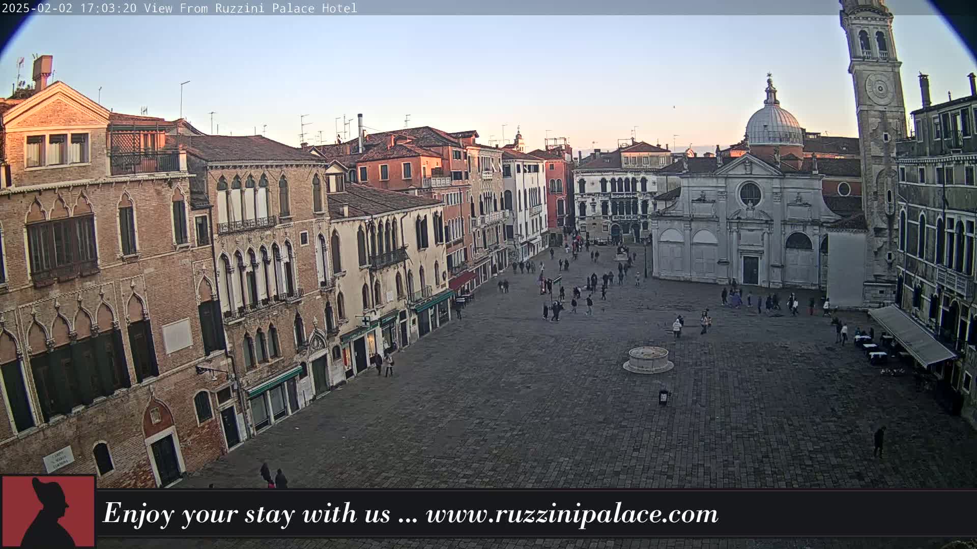 A large, cobblestone square in Venice is sparsely populated with people, surrounded by aging, multi-story buildings under a clear, twilight sky.